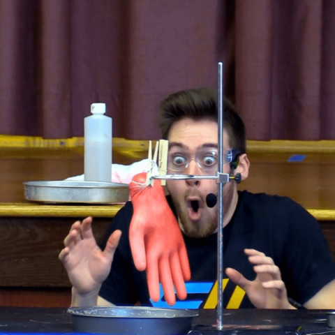 Talewise Science Lab Photo of a man with a surprised expression looking at a glove expanding during an experiment