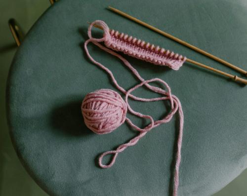 A green chair with wooden knitting needles and pink yarn